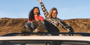 two woman sitting on top of white vehicle under blue sky during daytime